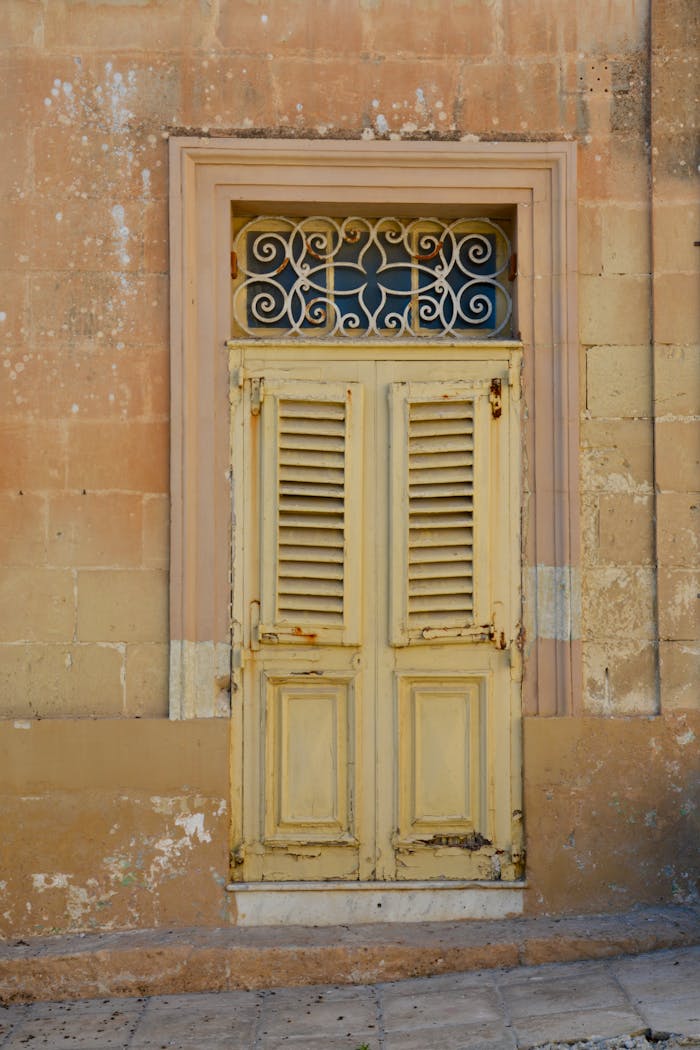 Old weathered yellow door on a Mediterranean building in Malta, showcasing vintage charm.